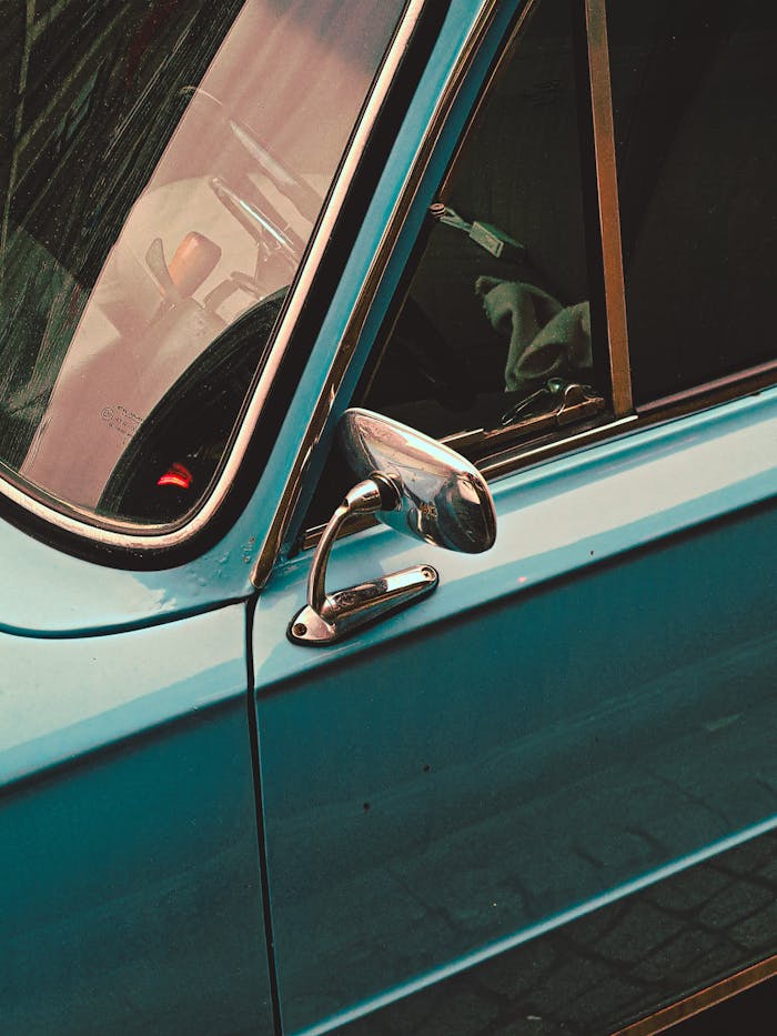 Close-up of a vintage car's blue door with chrome handle and mirror.