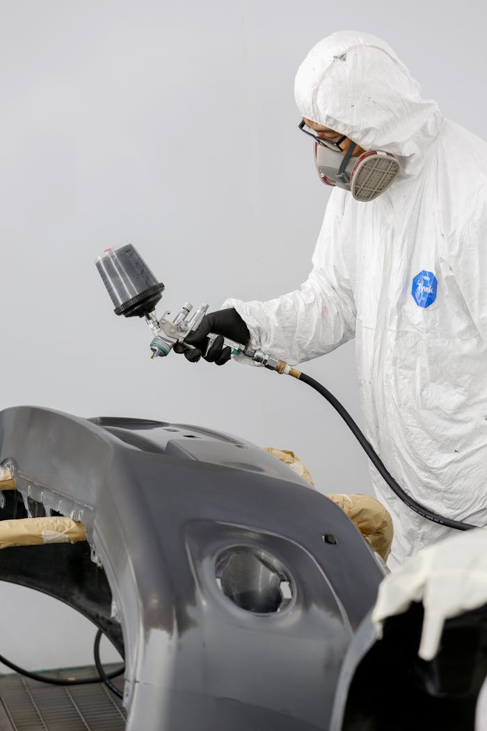Services Technician in protective gear spray painting a car bumper.