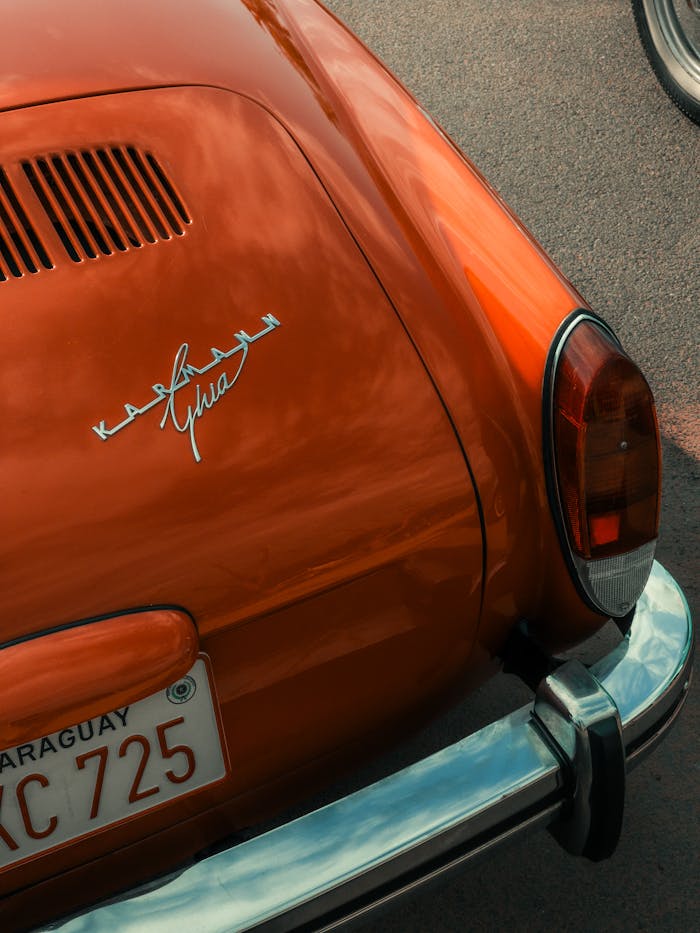 Close-up of a vintage orange car's tail showing emblem and license plate.