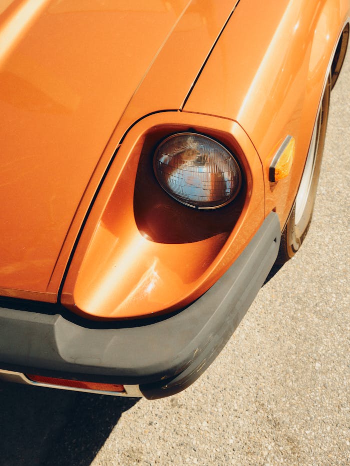Detailed view of a classic orange car headlight in bright sunlight, showcasing retro design.