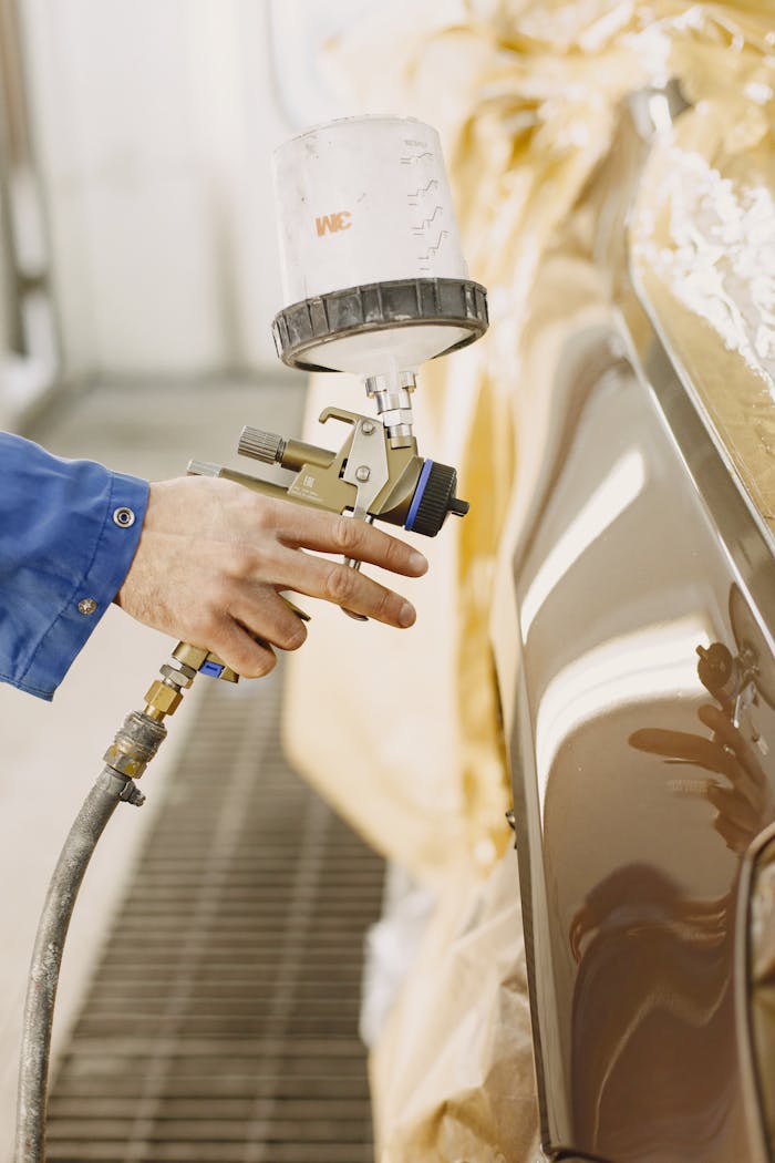 Services A technician spray paints a car with a paint spray gun in a workshop.